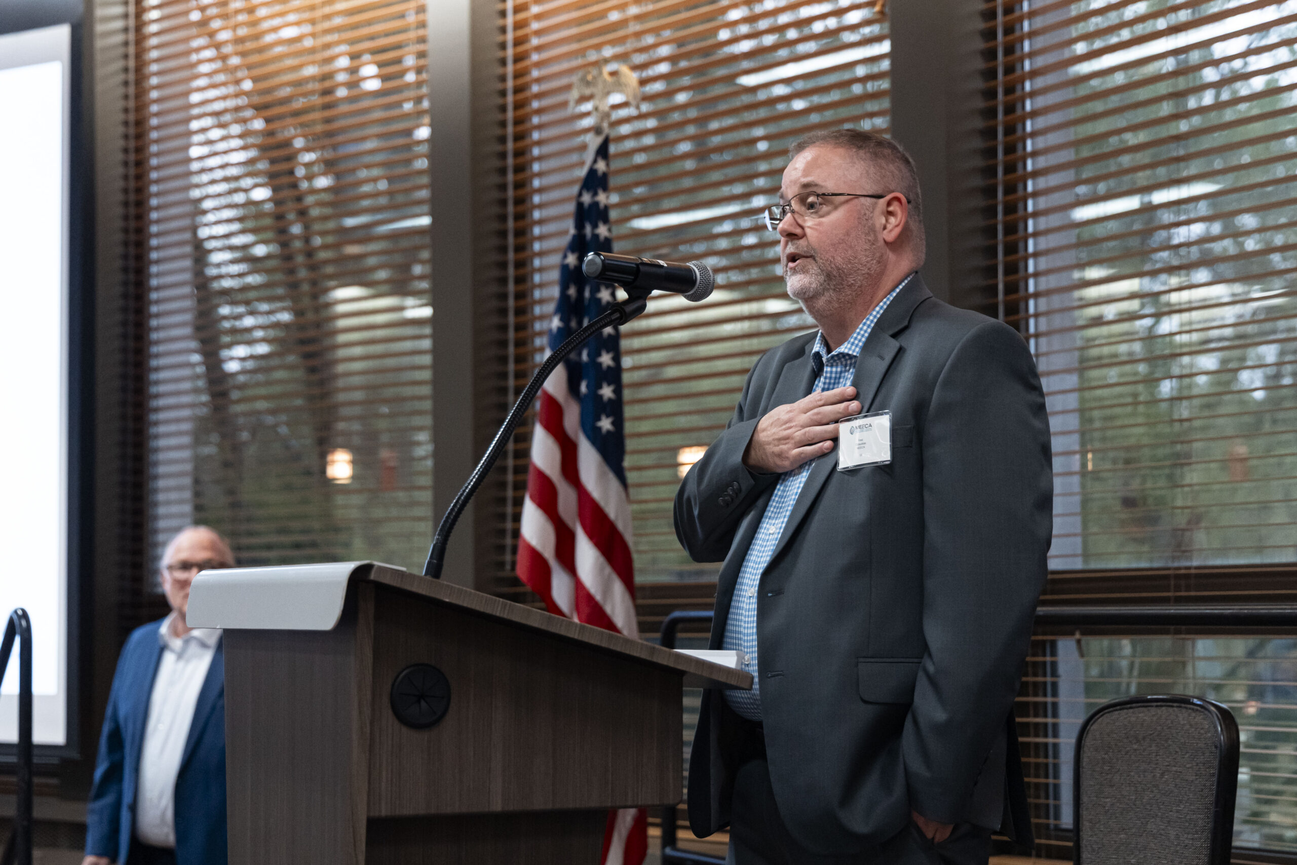 A MEECA member speaking at the podium at the MEECA award ceremony, American flag beside him.