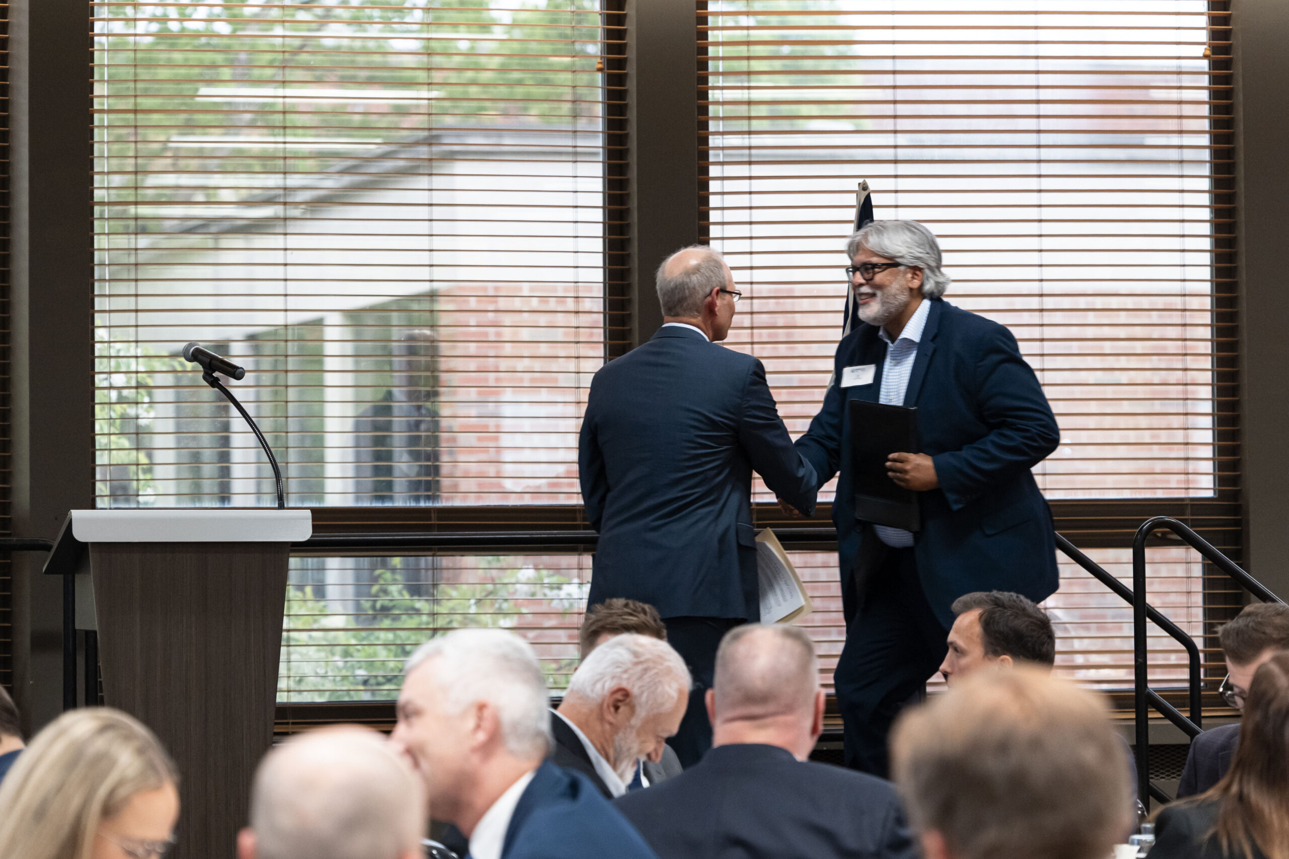 MEECA award ceremony: two members shaking hands on stage in front of a seated audience.